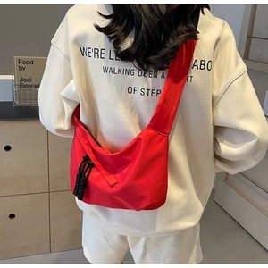 Détail du sac bandoulière rouge demi-lune avec nœud de fermeture sur fond beige neutre