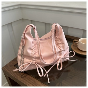 Pink nylon tote bag with drawstring sides, side bows and silver chain on wood table