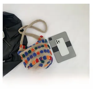 Size comparison of beige bucket bag with colorful pom-poms next to a tablet and smartphone