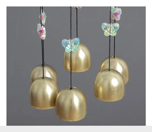 Detailed macro shot of matte golden copper wind chime bells with iridescent butterfly charms