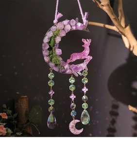 Macro detail of crescent moon pendant with pink deer and purple crystal bead tassels