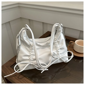 Detail of white hobo bag with gathered pleats and decorative bows on wooden desk