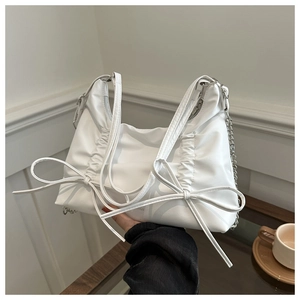 Close-up of white leather tote bag featuring bow ribbon details and a silver chain strap