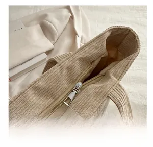 Detail shot of the smooth metal zipper on a beige corduroy tote bag showing texture