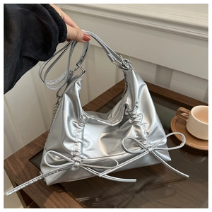 Close-up of silver pleated tote bag with bow details and versatile metallic chain strap
