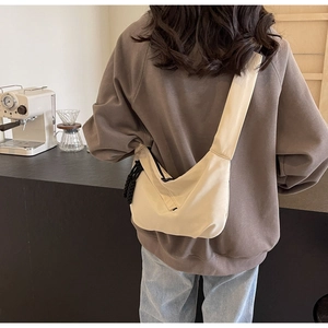 Close-up of beige half-moon crossbody bag with decorative rope knot details and wide strap