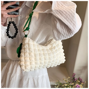Detail of cream bubble textured shoulder bag with green strap and floral charm