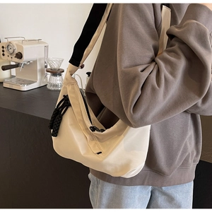 Detail of light beige crescent crossbody bag with woven zipper puller on a wide strap