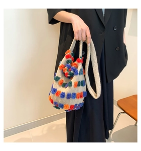 Détail du sac seau en tricot avec pompons colorés et bandoulière large porté par un mannequin