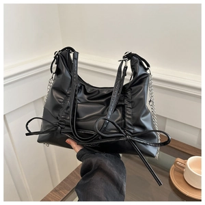 Detail showing black ruched bag with bow accents and silver chain in a lifestyle setting
