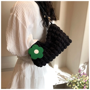 Detail of black popcorn texture shoulder bag with green flower charm on white dress