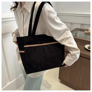 Close-up of black corduroy tote bag featuring vertical texture and dual front pockets