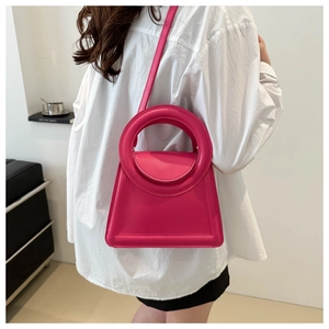 Fuchsia trapezoid leather handbag with circular handle shown on white shirt model