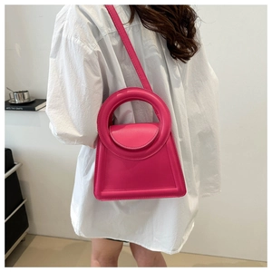 Model wearing a structured rose red handbag with large circular handle and trapezoid shape
