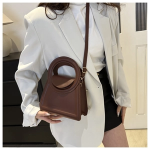 Close-up of a minimalist dark brown trapezoid handbag with a circular cutout handle