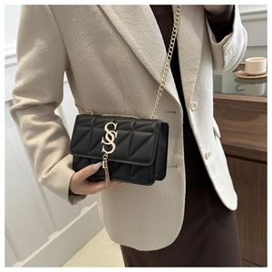 Détail du sac matelassé noir avec boucle dorée en S et finitions à pompons