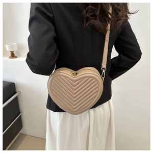 Detail of beige heart-shaped crossbody bag with chevron quilting and golden hardware