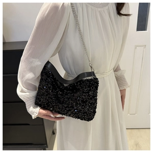 Close-up of black sequined shoulder bag with silver chain strap worn with a white skirt