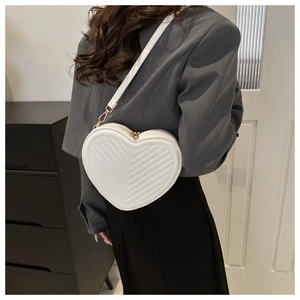 White heart-shaped quilted crossbody bag with gold hardware shown on a model
