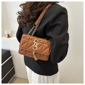 Détail d'un sac à bandoulière matelassé marron avec chaîne dorée et pompon décoratif