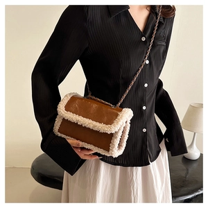 Detail of a brown leather crossbody bag featuring white faux shearling trim and chain strap