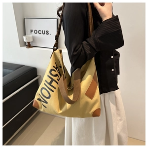 Detailed view of the yellow canvas tote bag showing fashion text and brown leather patches