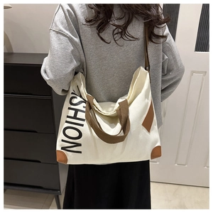 Rear view of model wearing a large cream canvas tote bag with brown straps and FASHION logo