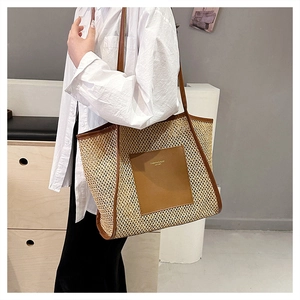 Detail of woven straw tote bag with brown leather trim and golden logo patch