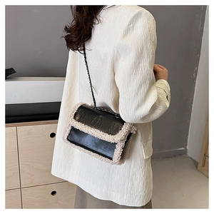 Detail of black matte leather shoulder bag with plush white faux fur trim and chain strap