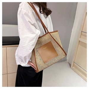 Dettaglio borsa tote in paglia intrecciata con finiture in pelle marrone e scritte dorate