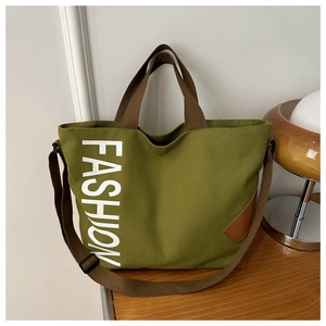 Detail of army green canvas tote bag with white FASHION text and brown handles