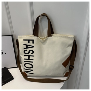 Close-up of cream canvas tote bag with brown leather handles and FASHION lettering