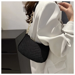Close-up of black herringbone textured shoulder bag with gold chain strap on model