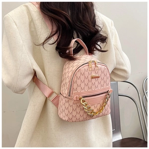 Close-up of pink mini backpack with M-pattern print and gold chain details on a model