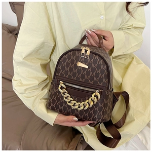 Close-up of brown mini backpack with M-pattern print and chunky gold chain detail