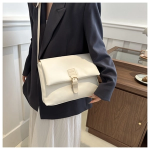On-shoulder view of a creamy white leather messenger bag with flap and buckle detail