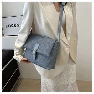 Close-up of matte grey-blue crossbody bag with strap and decorative buckle detail