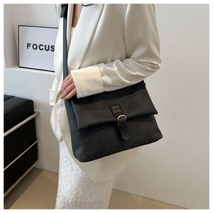 Close-up of vintage black matte leather crossbody bag with gold buckle on a white blazer