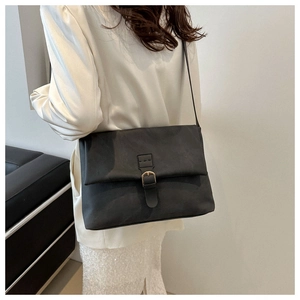Detail of a minimalist black crossbody bag with gold buckle on a stylish model