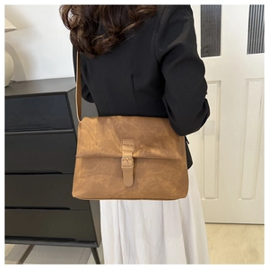Detailed side view of a brown leather crossbody bag worn by a model in a minimal setting