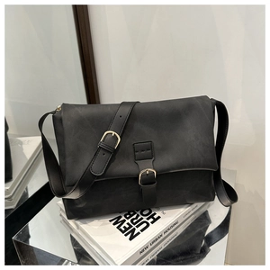 Close-up of black crossbody bag with matte texture and golden buckle on white books