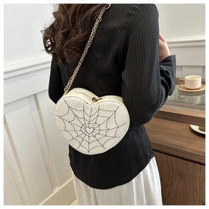 Detail of white heart-shaped crossbody bag featuring black spider web embroidery and chain