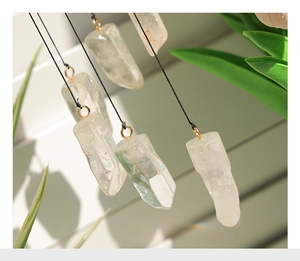 Detail of natural clear quartz pillar with gold metal ring and black cord on outdoor grid