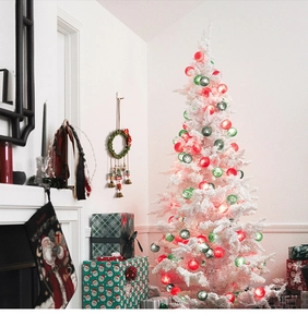 Detail of red and green string lights on a white Christmas tree with festive decor