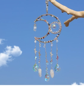 Detail of moon-shaped suncatcher with colorful crystals hanging outdoors against a blue sky