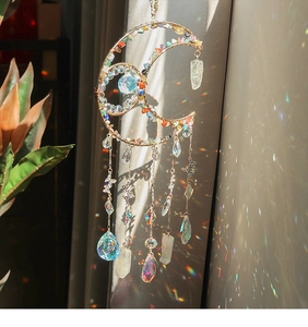 Moon-shaped suncatcher with colorful crystals casting a rainbow prism on curtains
