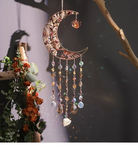 Detail of rose gold moon suncatcher with crystals and rainbow light on a branch