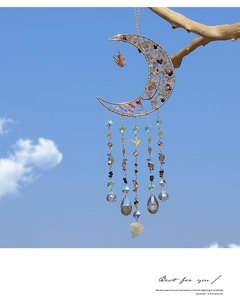 Detail of moon-shaped suncatcher with crystals and hummingbird pendant hanging outdoors