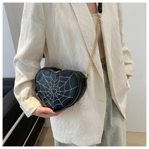 Macro shot of heart-shaped crossbody bag with white spider web embroidery and gold chain