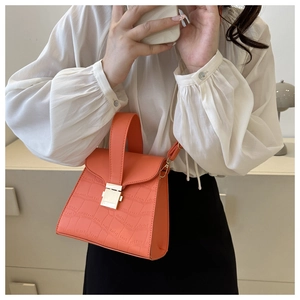 Detail of orange embossed crocodile pattern handbag with golden metal lock and shoulder strap